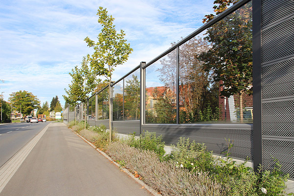 Lärmschutzwand aus Hlas an einer Straße erlaubt den Blick auf den dahinterliegenden Park